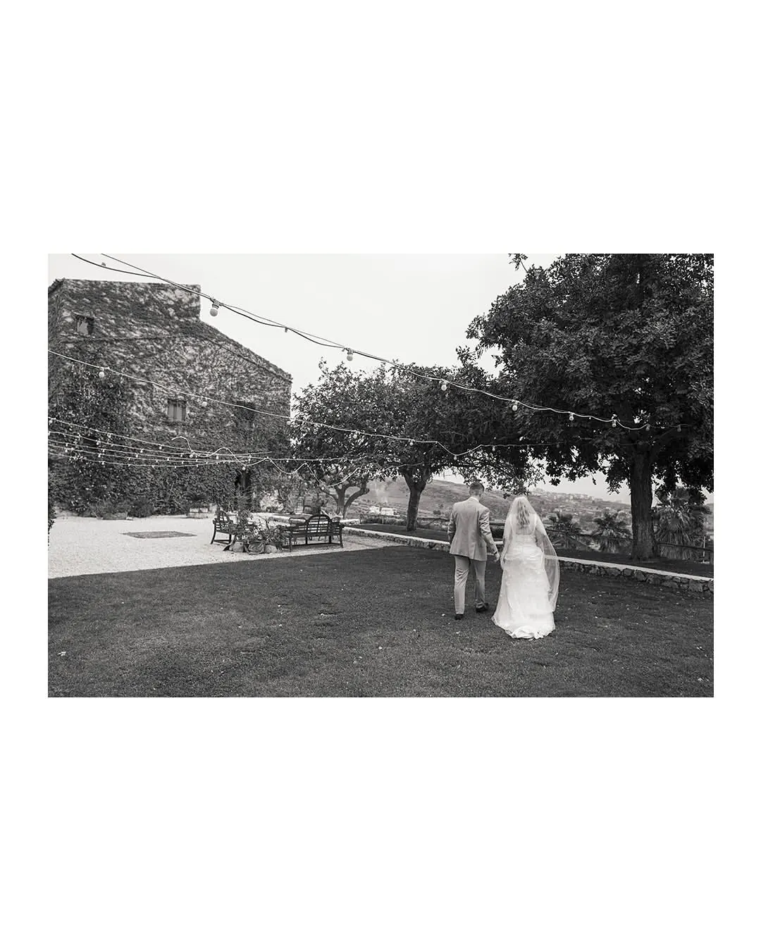 Newlyweds walking through the garden with festoon lights at the Agrigento wedding masseria